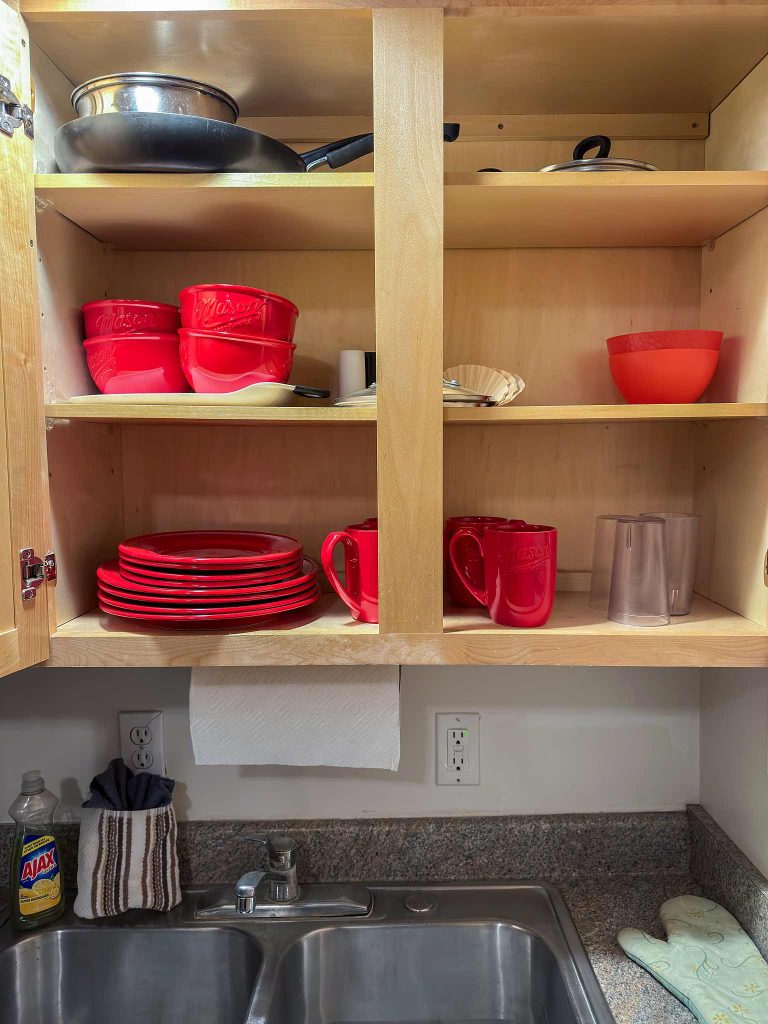 A kitchen cupboard full of bright red dishes available for our guests